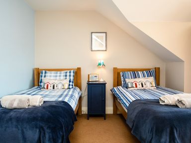 A bedroom with two single beds with striped bedding a blue nightstand with a lamp and radio at Upper Alnbank in Alnmouth