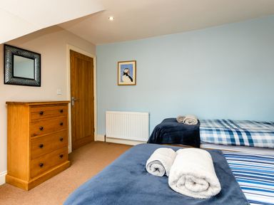 A bedroom with two single beds with towels on the beds a wooden chest of drawers and a door at Upper Alnbank in Alnmouth