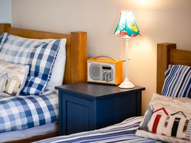 A bedroom with two wooden beds with striped bedding a blue nightstand with a floral lamp and a radio at Upper Alnbank in Alnmouth