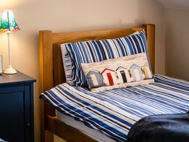 A bedroom with a wooden bed frame blue striped bedding and a nightstand with a lamp at Upper Alnbank in Alnmouth