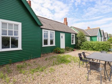 A gravel yard with outdoor table and chairs next to green wooden cottages at Sand Dune Cottage in Bamburgh