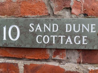 A house number plaque mounted on a brick wall at Sand Dune Cottage in Bamburgh