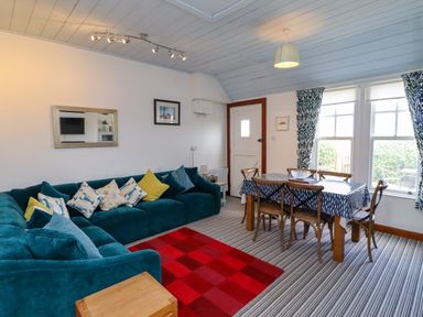 A living room with a blue sectional sofa and dining table with chairs at Sand Dune Cottage in Bamburgh