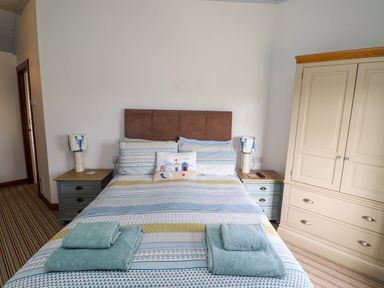 A bedroom with a bed with folded towels bedside tables with lamps and a wardrobe at Sand Dune Cottage in Bamburgh