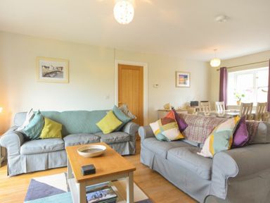 A living room with two sofas cushions a coffee table and a dining table with chairs at Schooner Court No1 in Alnmouth