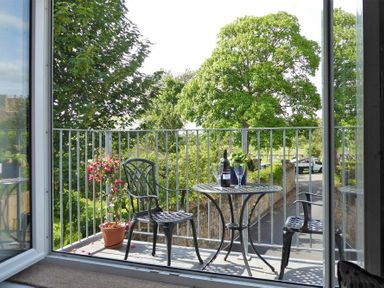 A balcony with two chairs a round table with wine and glasses and a potted plant at Schooner Court No1 in Alnmouth