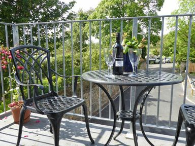 A metal table with a bottle of wine two wine glasses and a plant on a balcony with metal railing and a metal chair at Schooner Court No1 in Alnmouth