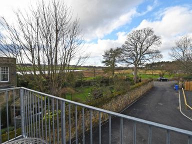 View of a paved driveway with parked car a stone wall leafless trees and grassy fields at Schooner Court No1 in Alnmouth