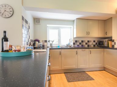 A kitchen with cream cabinets black countertop a window a microwave toaster kettle and a bottle on a tray at Schooner Court No1 in Alnmouth