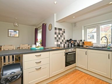 A kitchen with cabinets oven sink and a dining area with chairs at Schooner Court No1 in Alnmouth
