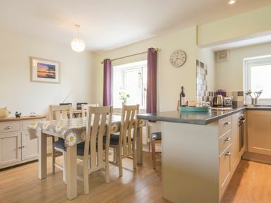 A dining area with a table and chairs next to a kitchen counter with appliances and window at Schooner Court No1 in Alnmouth