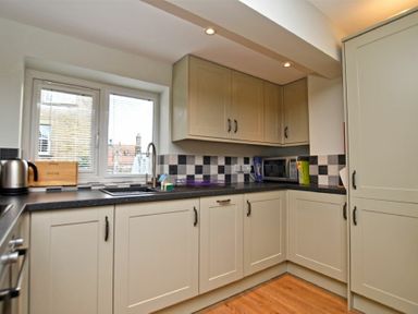 A kitchen with beige cabinets black countertop checkered backsplash and a window at Schooner Court No1 in Alnmouth