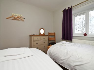 A bedroom with two single beds white bedding a chest of drawers wooden chair and purple curtains at Schooner Court No1 in Alnmouth