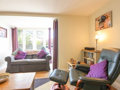 A living room with a sofa and armchair with purple cushions at Schooner Court No2 in Alnmouth