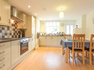 A kitchen with cabinets an oven a dining table with chairs and a window at Schooner Court No2 in Alnmouth