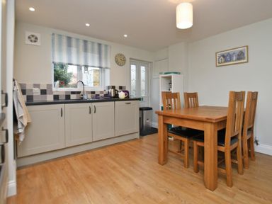A kitchen with wooden dining table and chairs next to gray cabinets and a window at Schooner Court No2 in Alnmouth