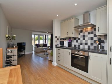 A kitchen with appliances and checkered backsplash next to a living room with sofas and a television at Schooner Court No2 in Alnmouth