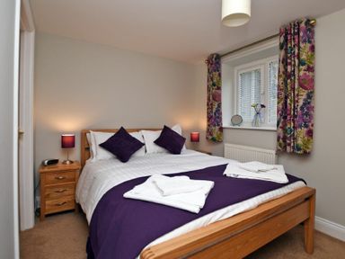 A bedroom with a wooden bed frame purple cushions and floral curtains at Schooner Court No2 in Alnmouth