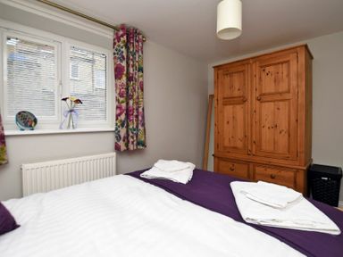 A bedroom with a bed, floral curtains, a wooden wardrobe, and a window with blinds at Schooner Court No2 in Alnmouth