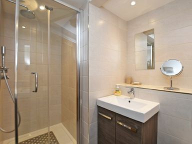 A bathroom with a glass shower enclosure and a sink with a mirror above at Schooner Court No2 in Alnmouth