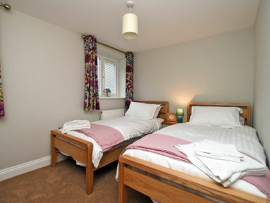 A bedroom with two single beds a nightstand with a lamp and clock and floral curtains at Schooner Court No2 in Alnmouth