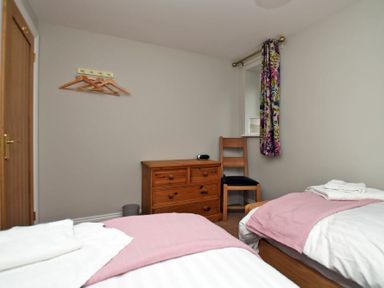 A bedroom with two single beds a wooden chest of drawers a wooden chair and a window with floral curtains at Schooner Court No2 in Alnmouth