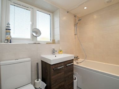 A bathroom with a toilet sink with cabinet and bathtub with shower at Schooner Court No2 in Alnmouth