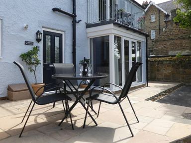 A patio area with a black round table and four chairs outside a building with a black door and glass balcony at Schooner Court No2 in Alnmouth