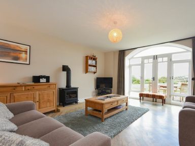 A living room with a wooden coffee table a wood stove a TV and large arched windows at Sea Breeze in Newton-by-the-Sea