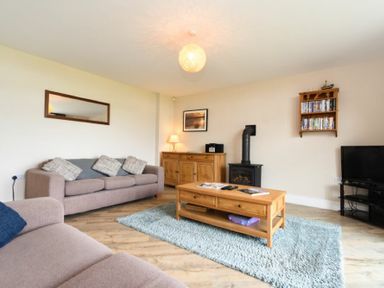 A living room with two sofas a wooden coffee table a wood burning stove and a television at Sea Breeze in Newton-by-the-Sea