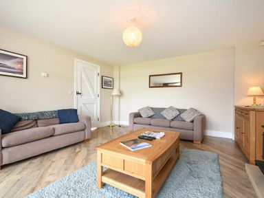 A living room with two sofas a wooden coffee table a floor lamp and a sideboard at Sea Breeze in Newton-by-the-Sea