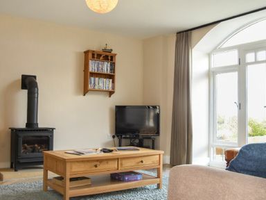 A living room with a wood stove a wooden coffee table and a TV near a large window at Sea Breeze in Newton-by-the-Sea