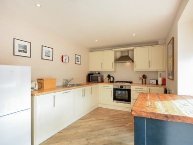 A kitchen with white cabinets wooden countertops and framed pictures on the wall at Sea Breeze in Newton-by-the-Sea