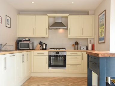 A kitchen with cream cabinets a stove microwave kettle and a blue island at Sea Breeze in Newton-by-the-Sea