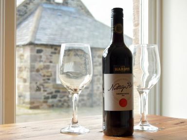 A bottle of red wine and two empty wine glasses on a wooden table in front of a window with a stone building outside at Sea Breeze in Newton-by-the-Sea