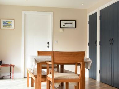 A dining area with a wooden table and chairs near white door and blue cupboards at Sea Breeze in Newton-by-the-Sea