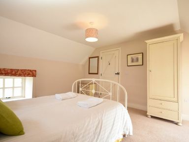 A bedroom with a metal bed frame a wardrobe a chest of drawers and a window with a red valance at Sea Breeze in Newton-by-the-Sea