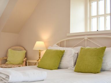 A bedroom with a bed with green cushions and a folded towel a chair with a green cushion and a lamp on a side table at Sea Breeze in Newton-by-the-Sea