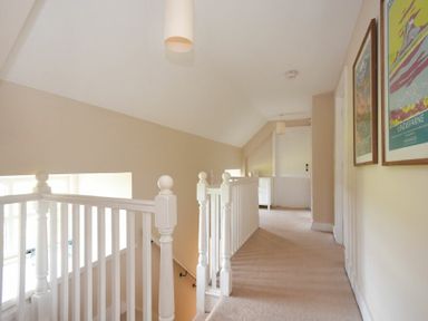 A hallway with white banisters carpeted floor and framed pictures on the wall at Sea Breeze in Newton-by-the-Sea