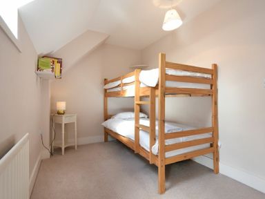 A bedroom with a wooden bunk bed a small white bedside table with a lamp and books on a wall shelf at Sea Breeze in Newton-by-the-Sea