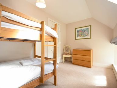 A bedroom with wooden bunk beds a wooden chest of drawers a chair and a framed picture on the wall at Sea Breeze in Newton-by-the-Sea