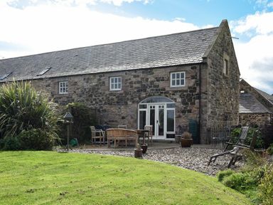 A stone building with a slate roof and outdoor seating area with tables and chairs at Sea Breeze in Newton-by-the-Sea