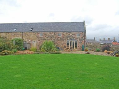 A stone house with a slate roof and a green lawn with garden furniture at Sea Breeze in Newton-by-the-Sea