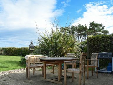 An outdoor patio with wooden chairs and a table next to a barbecue grill and plants at Sea Breeze in Newton-by-the-Sea