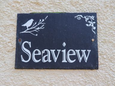 A black sign with the word Seaview and white bird and branch decorations on a textured beige wall at Seaview Howick Craster