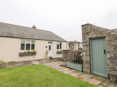 An exterior view of a single-story house with a front door and two windows with flower boxes and a stone wall with a green wooden door at Seaview Howick in Craster