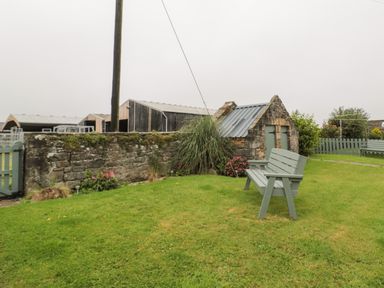 A garden with green benches and stone buildings behind a stone wall at Seaview Howick in Craster