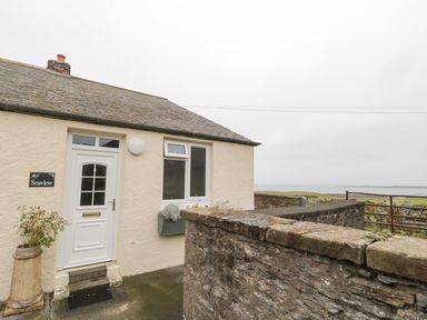 The exterior front entrance of a cottage with a white door a window a flower box and a stone wall overlooking a coastal landscape at Seaview Howick in Craster