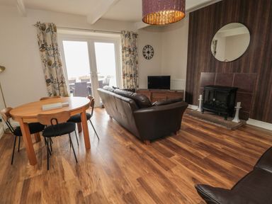 A living room with a dining table and chairs a sofa a television and a fireplace at Seaview Howick in Craster