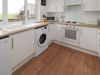 A kitchen with white cabinets wooden countertops a washing machine oven stovetop microwave and a window at Seaview Howick in Craster